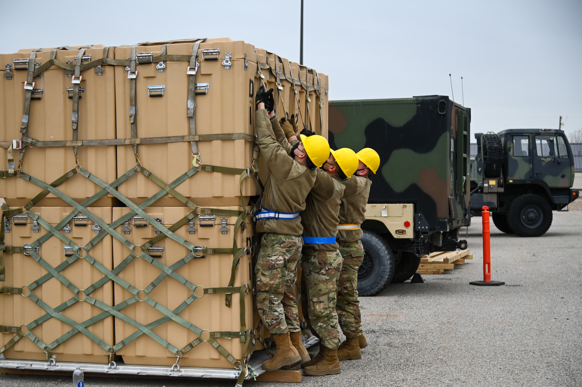 Three Airmen tightening the straps down on cargo sitting on a pallet.