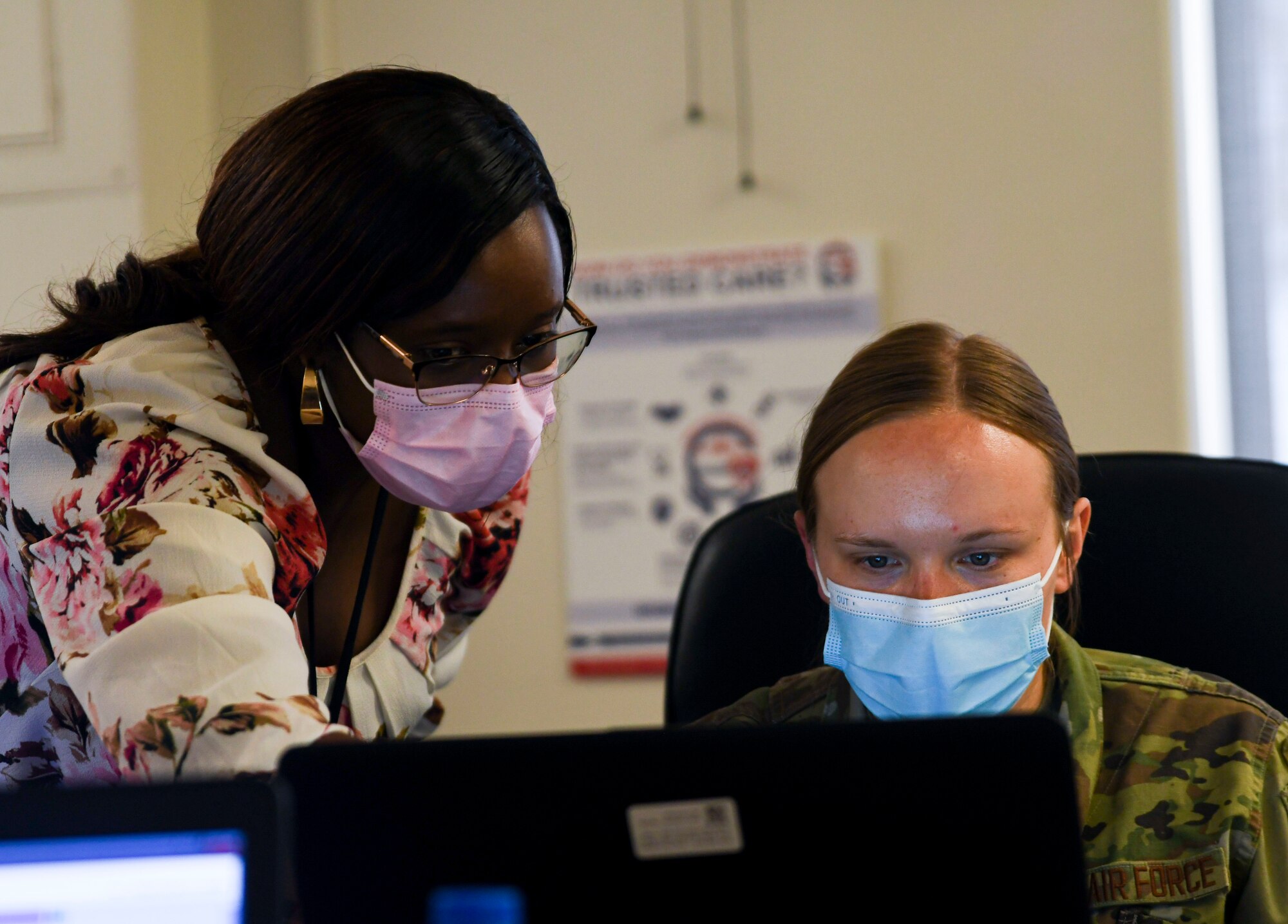 A photo of a civilian pointing to a computer screen next to an airmen