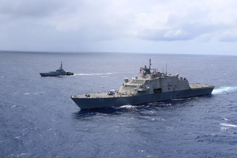 Navy ships sail in formation across the sea.