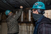 Shop 64 Woodcrafter Robert Penland and Shop 64 Woodcrafter Matthew Thornton use the Hammer Activated Measurement System for Testing and Evaluating Rubber (HAMSTER) on the hull of a submarine.