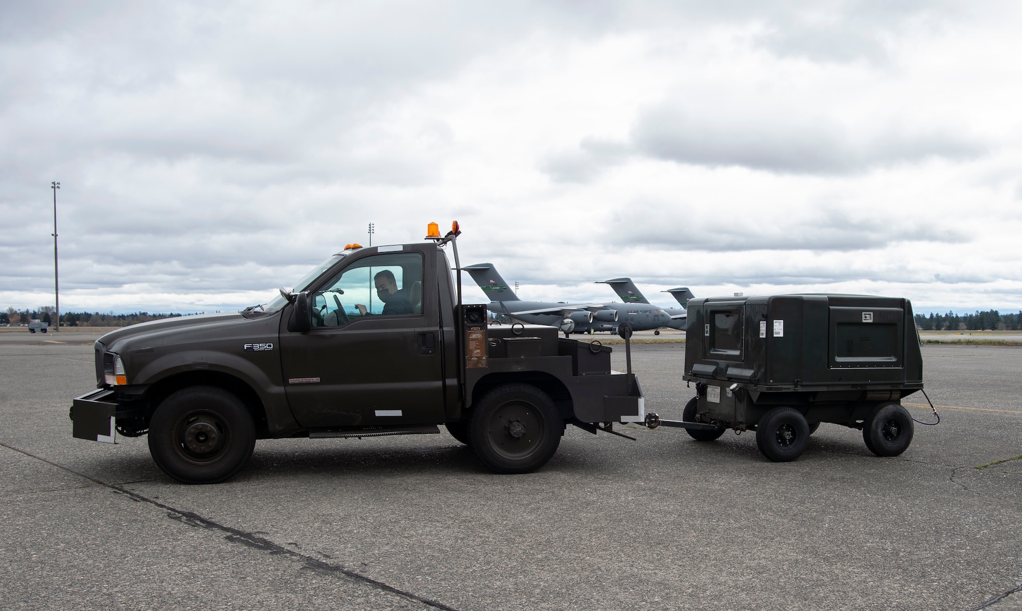 U.S. Air Force Airman 1st Class Sean Gilbert, 62nd Maintenance Squadron Aerospace Ground Equipment Flight apprentice, tows a generator at Joint Base Lewis-McChord, Washington, April 7, 2021. The service, pick-up and delivery (SPUDS) section of the 62nd MXS AGE flight transports equipment to and from the flightline to assist in the inspection and repair of C-17 Globemaster IIIs at McChord Field. (U.S. Air Force photo by Senior Airman Tryphena Mayhugh)
