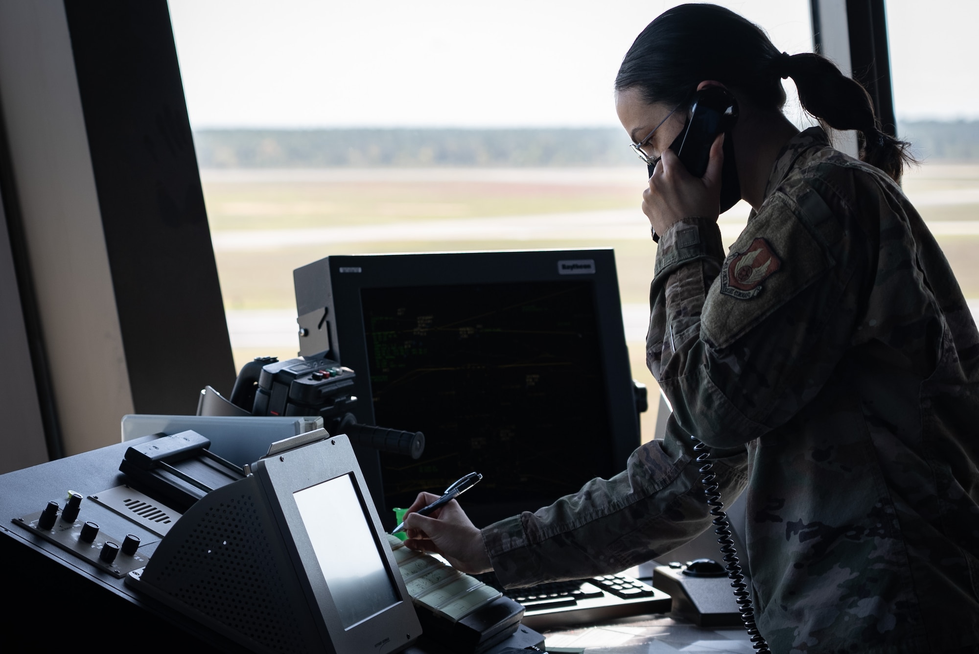 Female Airman answers phone and writes with a pen.