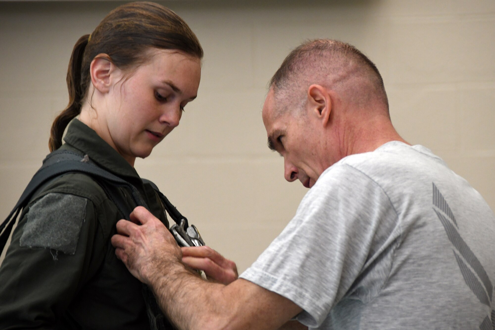 Senior Airman Micaiah Walker, a loadmaster assigned to the 757th Airlift Squadron, watches as Master Sgt. Phillip Walsh, Aircrew Flight Equipment Non-Commissioned Officer in Charge assigned to the 910th Operations Support Squadron, buckles her parachute harness clasp as part of a water landing parachute harness drag and release exercise during an aircrew water survival refresher training event at Youngstown State University’s Beeghly Natatorium Olympic Swimming Pool, April 11, 2021.