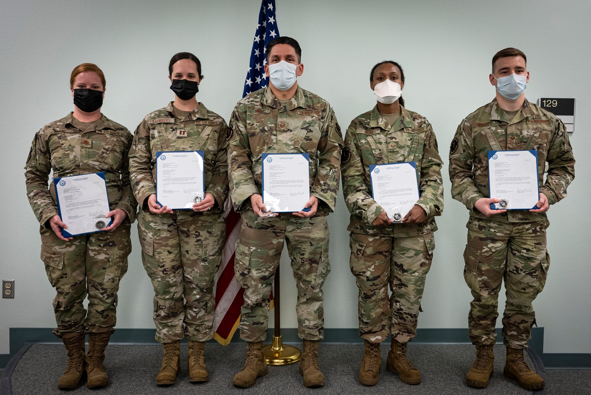 Five medical Airmen hold awards in front of U.S. flag.