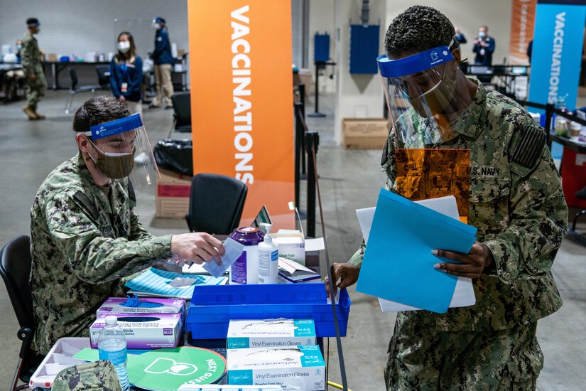 Navy sailors wearing face masks refill COVID-19 vaccine supplies.