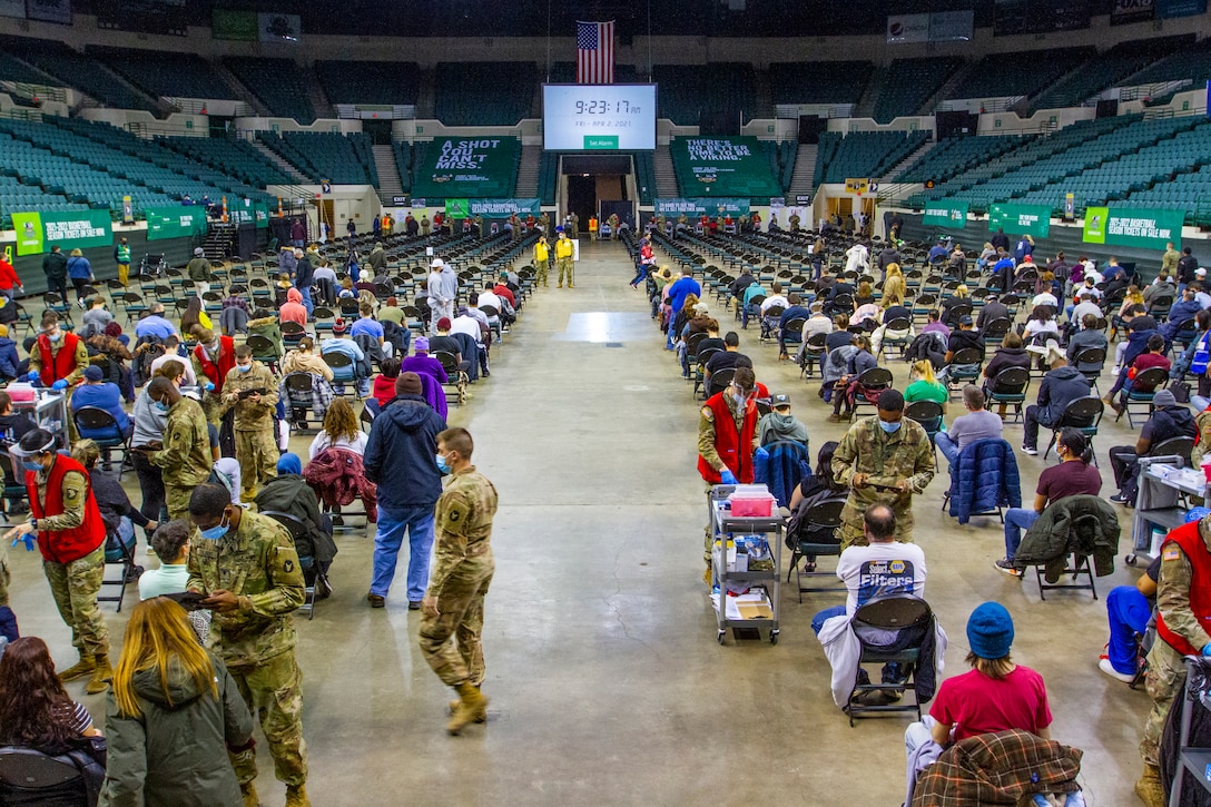 Army soldiers wearing face masks and gloves administer their one hundred thousandth dose of COVID-19 vaccines.