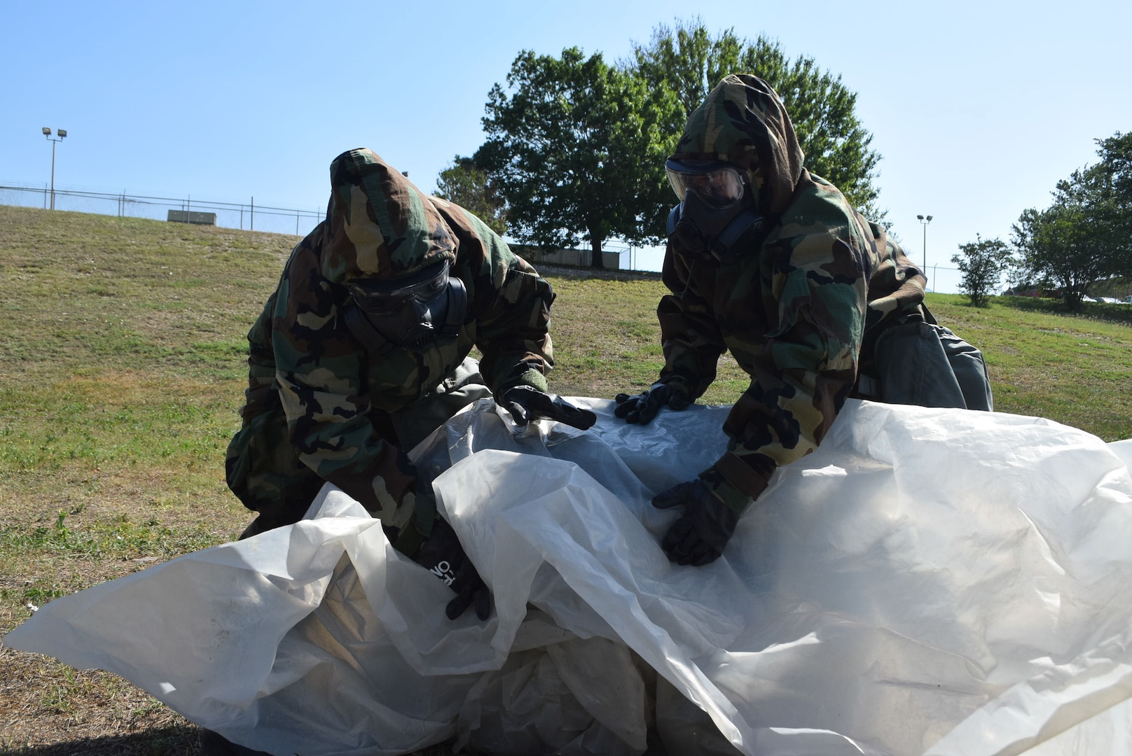 Senior Airman Jennifer Martinez and Senior Airman Ashley Garcia, 433rd Force Support Squadron, assess and cover a contaminated container for transport during a field training exercise, April 10, 2021, at Joint Base San Antonio-Lackland, Texas. Participants donned mission-oriented protective posture gear to transport simulated hazardous material. (U.S. Air Force photo by Tech. Sgt. Mike Lahrman)