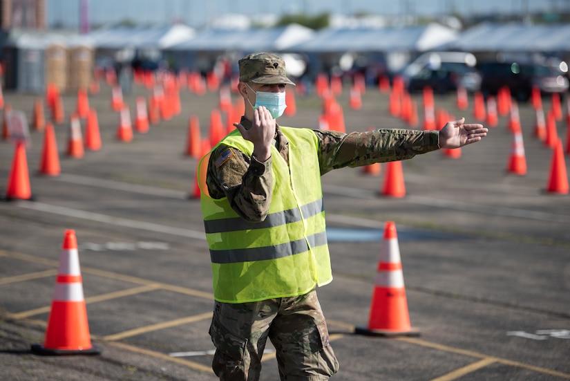 U.S. Army Spc. Logan Kilmon of the Kentucky Army National Guard directs traffic at Kentucky’s largest drive-through COVID-19 vaccination clinic at Cardinal Stadium in Louisville, Ky., April 12, 2021. More than 30 Soldiers and Airmen from the Kentucky Army and Air National Guard are providing direct support to the clinic, which can vaccinate up to 4,000 patients a day. (U.S. Air National Guard photo by Dale Greer)