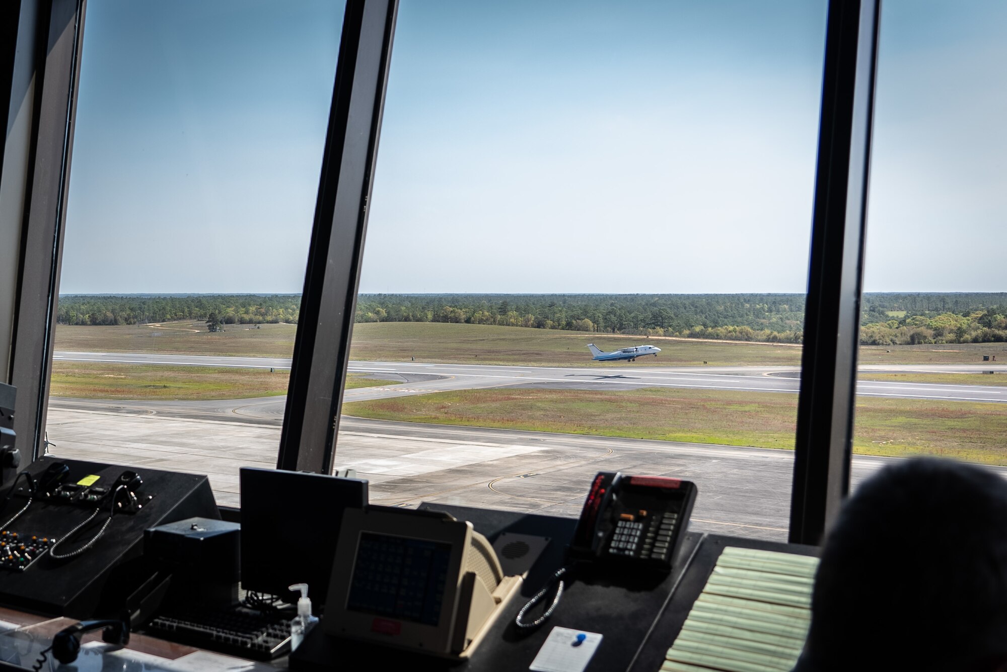 Aircraft takes off from runway as seen through window of control tower.