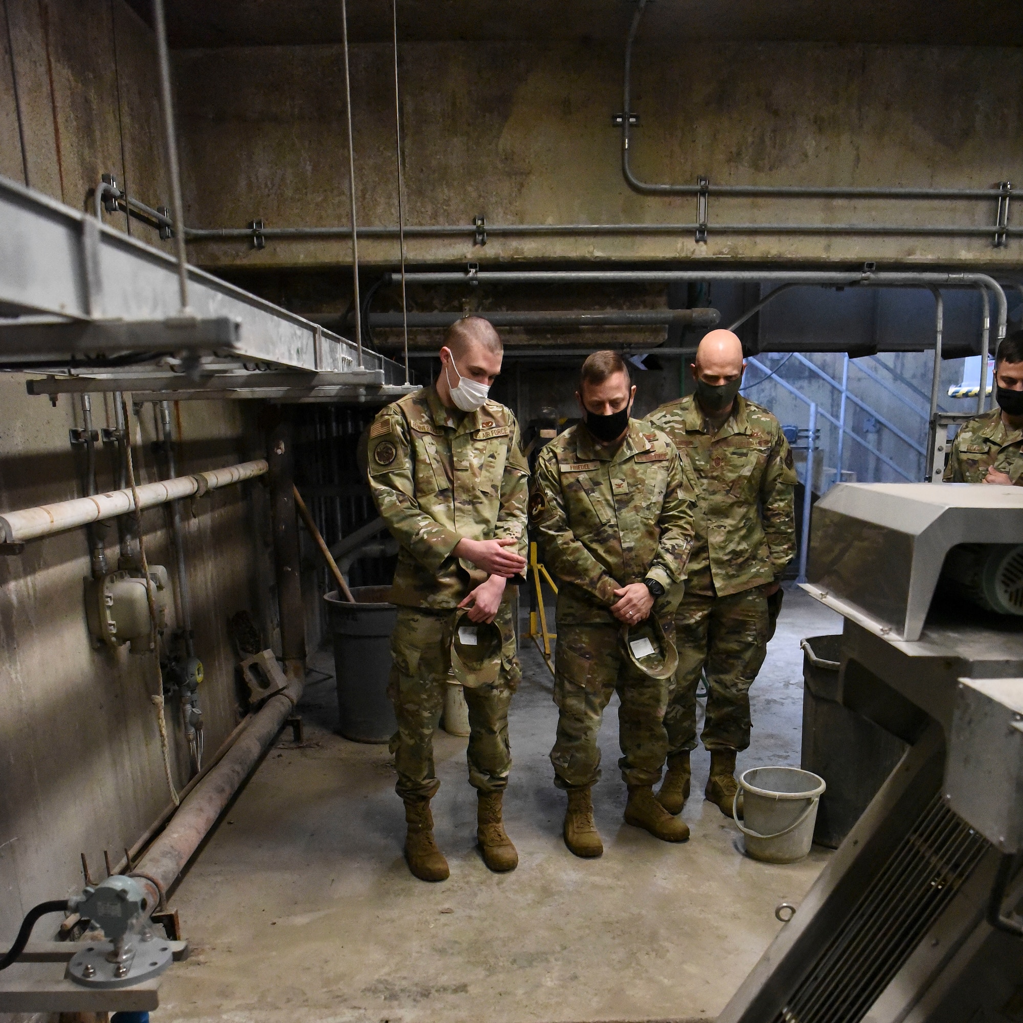 Three men in uniform stand looking at equipment.