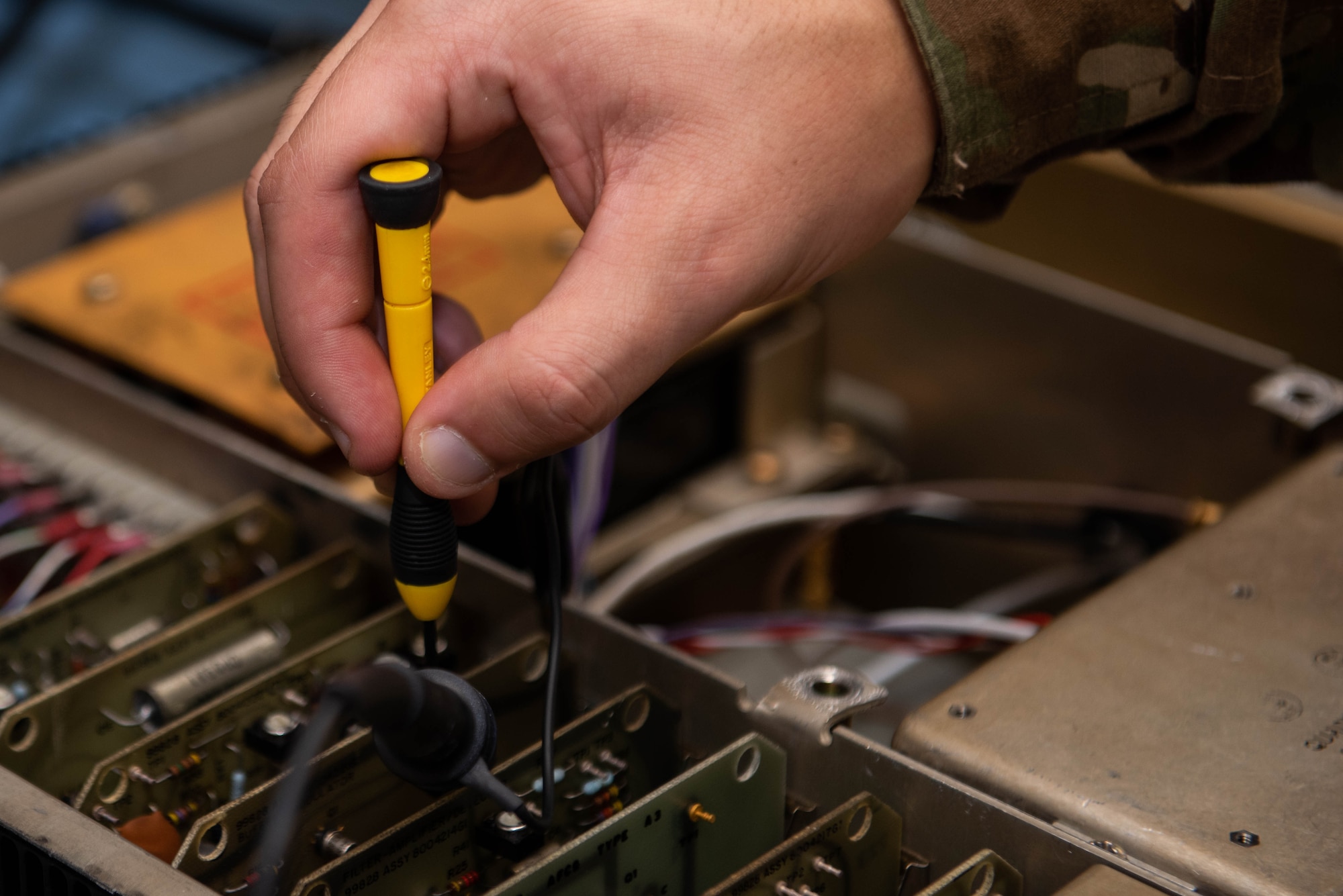 A closeup of a an Airman's hand fixing a delicate part of a radio