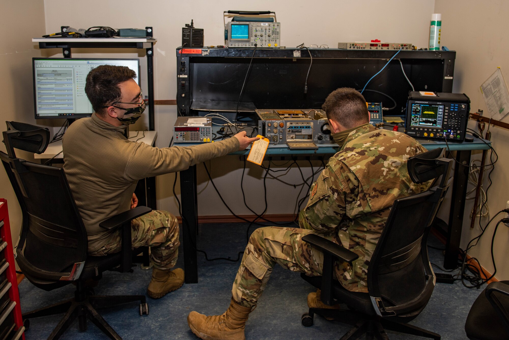 Two seated Airmen repair radio equipment on a workbench