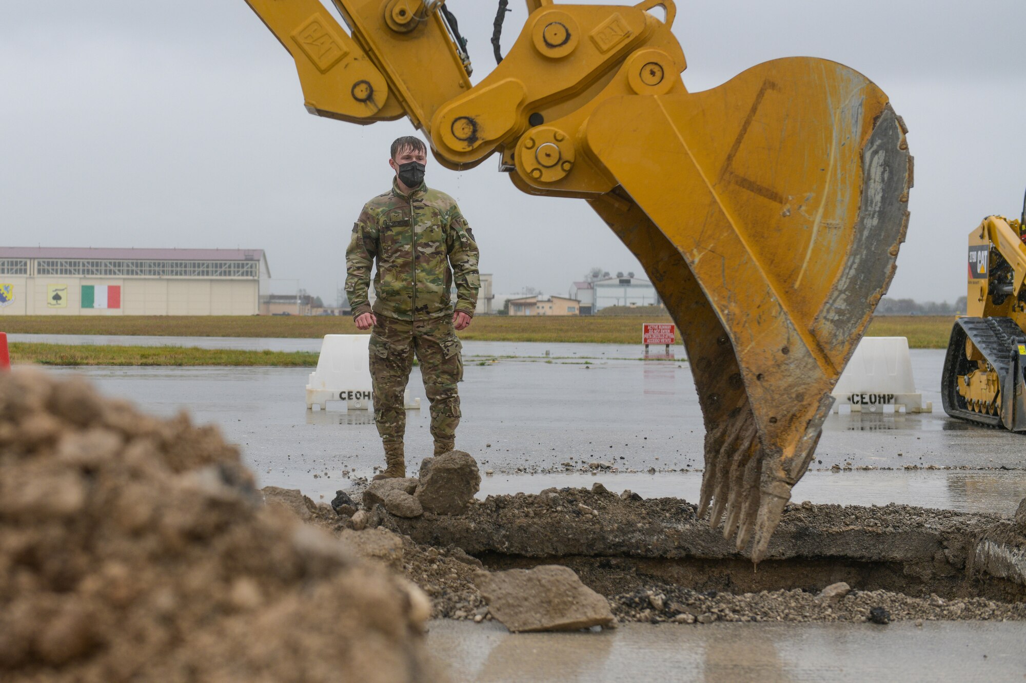 Airman 1st Class Brenden Kazmierczak, 31st Civil Engineer Squadron water and fuels technician, watches an excavator dig a crater during a base defense readiness exercise at Aviano Air Base, Italy, April 12, 2021. The 31st CES conducted Rapid Airfield Damage Repair (RADR) during the exercise, creating a stable base for a concrete mixture to pour into the crater. (U.S. Air Force photo by Airman 1st Class Brooke Moeder)