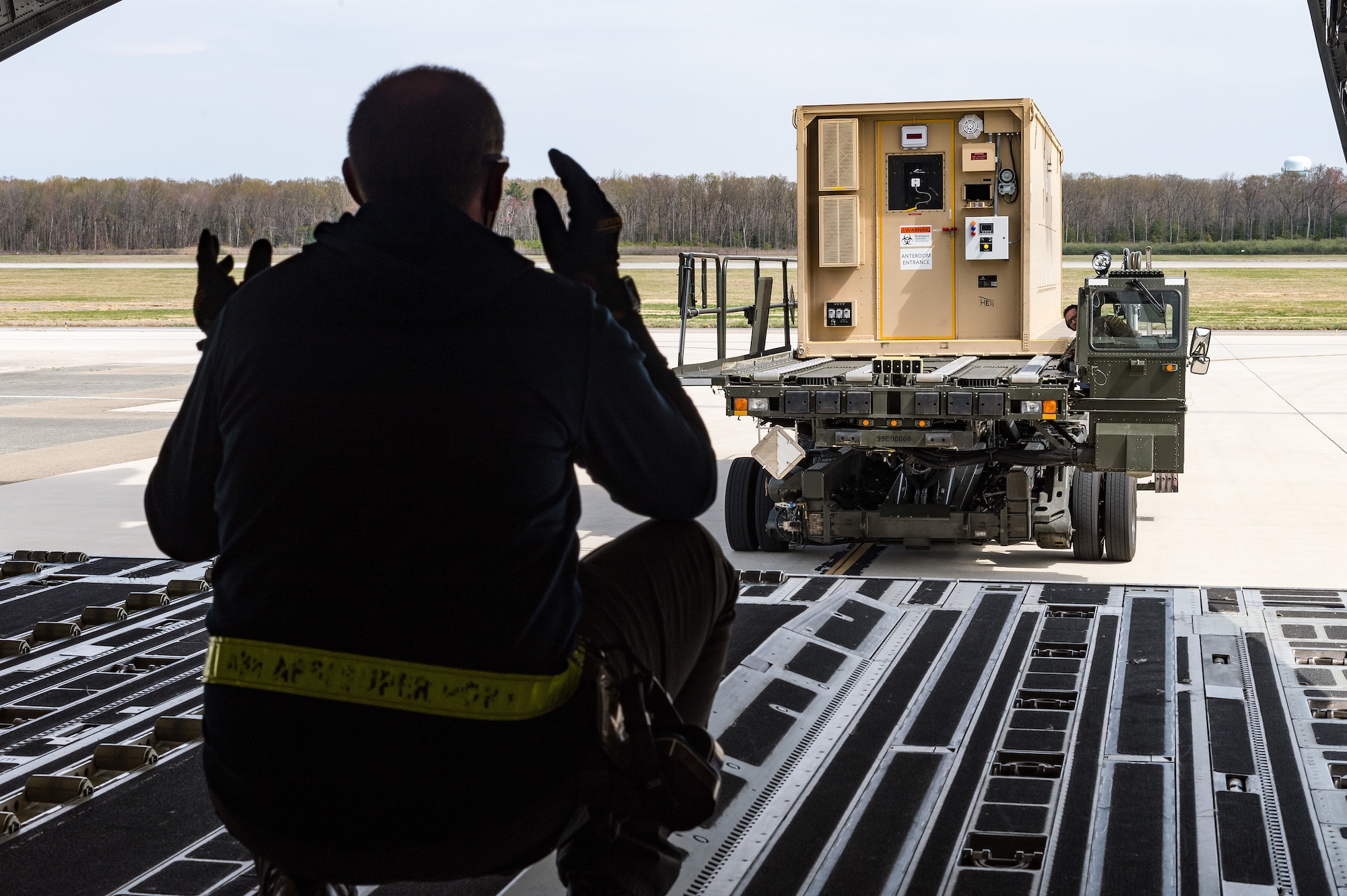 A 436th Aerial Port Squadron ramp service specialist marshals a Negatively Pressurized Conex onto a C-17 Globemaster III on Dover Air Force Base, Delaware, April 7, 2021. The 775th Expeditionary Aeromedical Evacuation Flight conducted training once the NPC was loaded on the aircraft. (U.S. Air Force photo by Roland Balik)