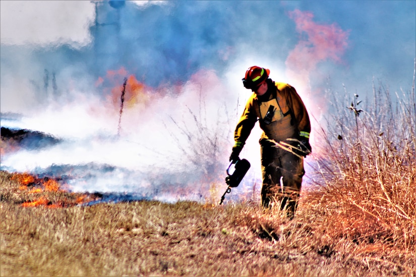 A man in firefighter gear burns grass.