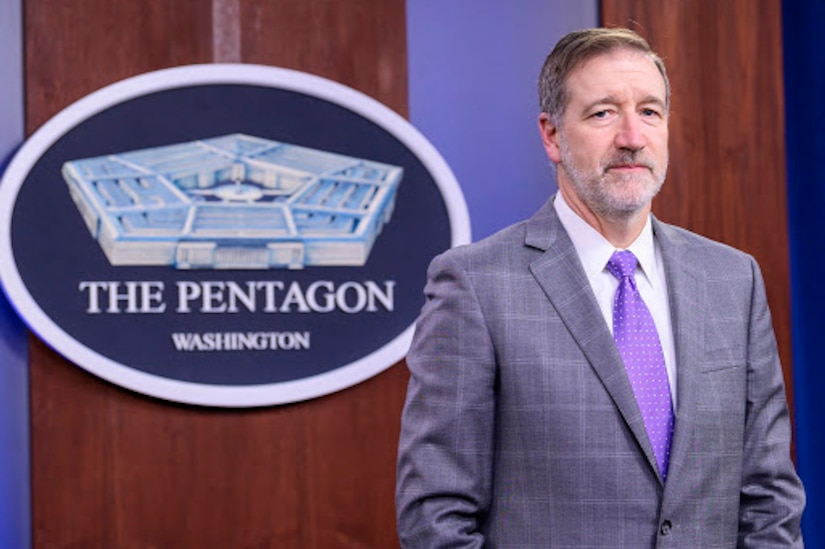 A man stands in front of a sign indicating that he is at the Pentagon.