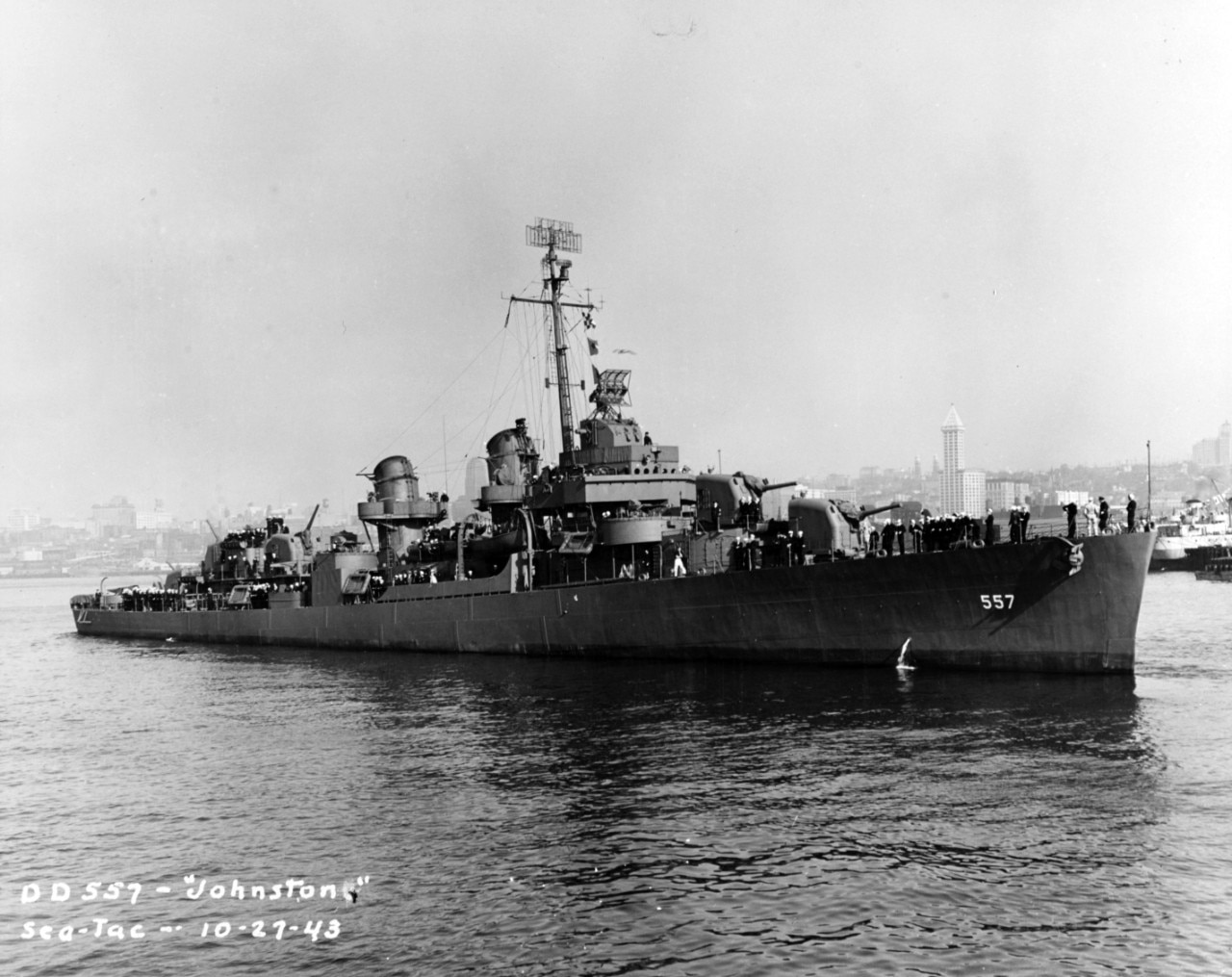 A large ship floats along the coastline; a cityscape is in the background.