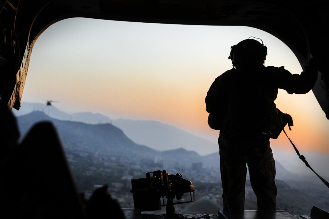 A soldier stands on the rear ramp of a helicopter.