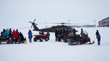 Community members of the City of Chevak watch from a safe distance as representatives from of the Alaska Department of Military and Veterans Affairs, the Department of Environmental Conservation, and the Department of Commerce, Community, and Economic Development load onto an Alaska Army National Guard UH-60 Black Hawk helicopter in Chevak, Alaska, April 9, 2021. Members of the Alaska Department of Military and Veterans Affairs, the Department of Environmental Conservation, and the Department of Commerce, Community, and Economic Development traveled to Western Alaska April 7-9 to meet with Tribal leaders and citizens in Bethel, Tuluksak, and Chevak to discuss disaster assistance measures and processes in light of recent emergencies that have occurred in the region, and in preparation for the upcoming flood season. (U.S. Army National Guard photo by Dana Rosso)