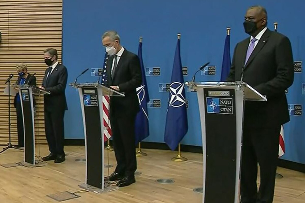 Three men stand on a stage and speak to reporters.