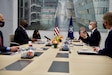 Two men stand beside each other next to U.S. and NATO flags.