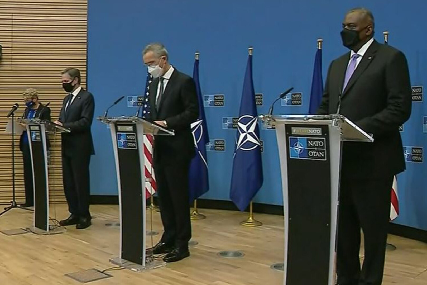 Three men stand on a stage and speak to reporters.