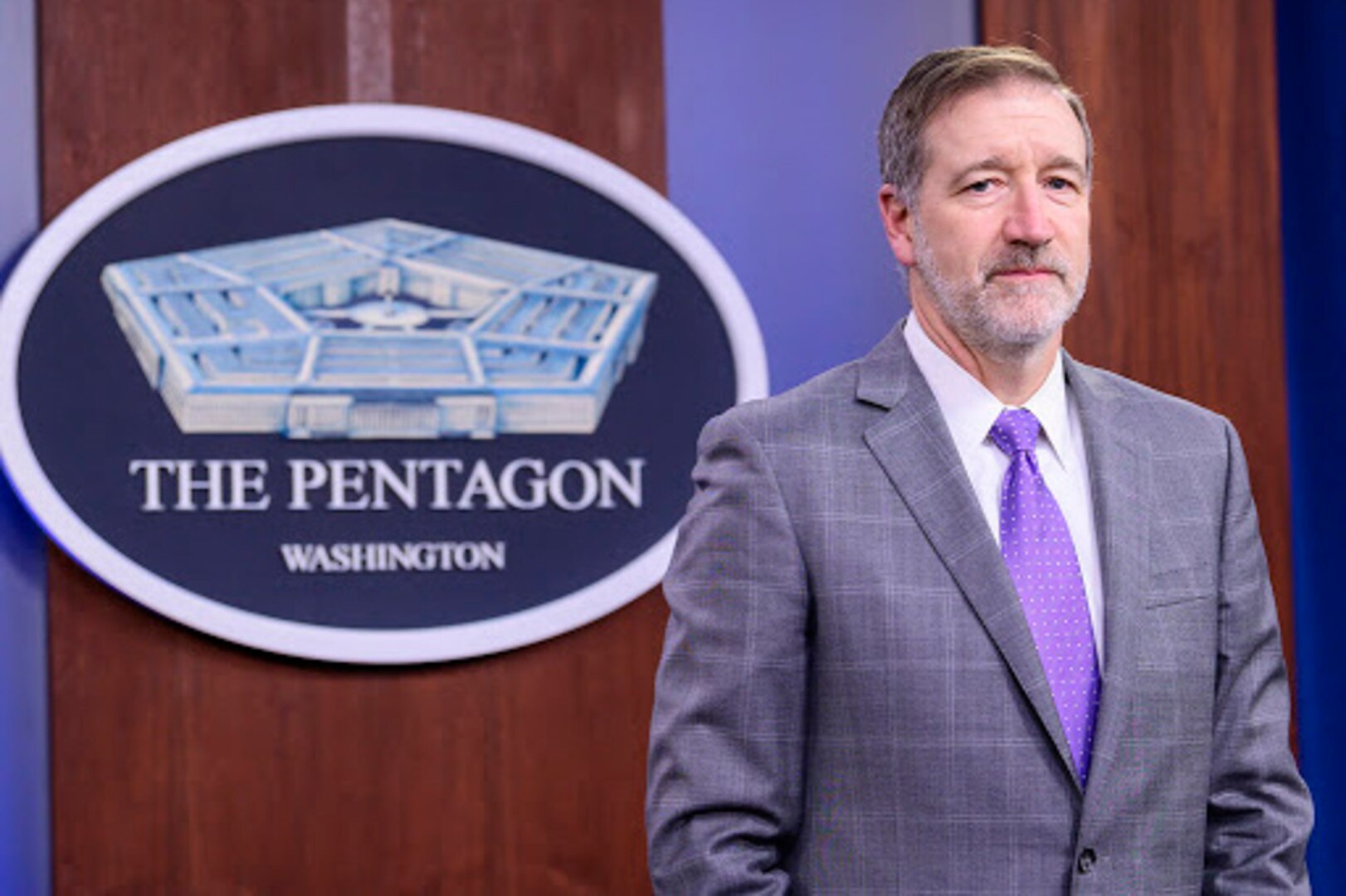 A man stands in front of a sign indicating that he is at the Pentagon.