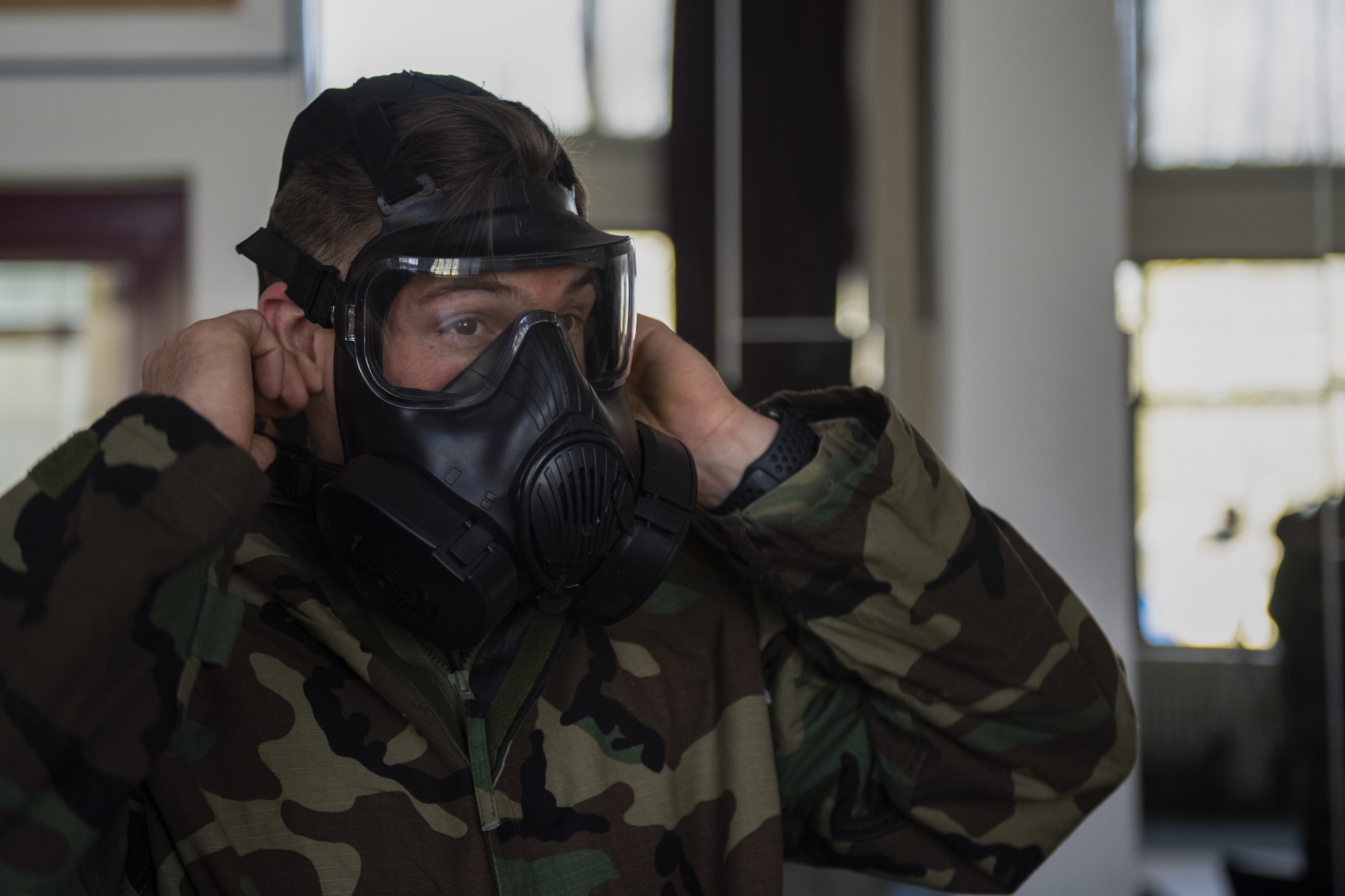 A U.S. Air Force Airman from the 702nd Munitions Support Squadron tightens his gask mask during the Mission Oriented Protective Posture gear portion of the chemical, biological, radiological and nuclear response training course at the 702nd MUNSS, April 13, 2021. The 702nd MUNSS is a geographically separated unit of the 52nd Fighter Wing, and as a result, its members must obtain training through the 52nd Civil Engineer Squadron's mobile CBRN training team.(U.S. Air Force photo by Senior Airman Ali Stewart)