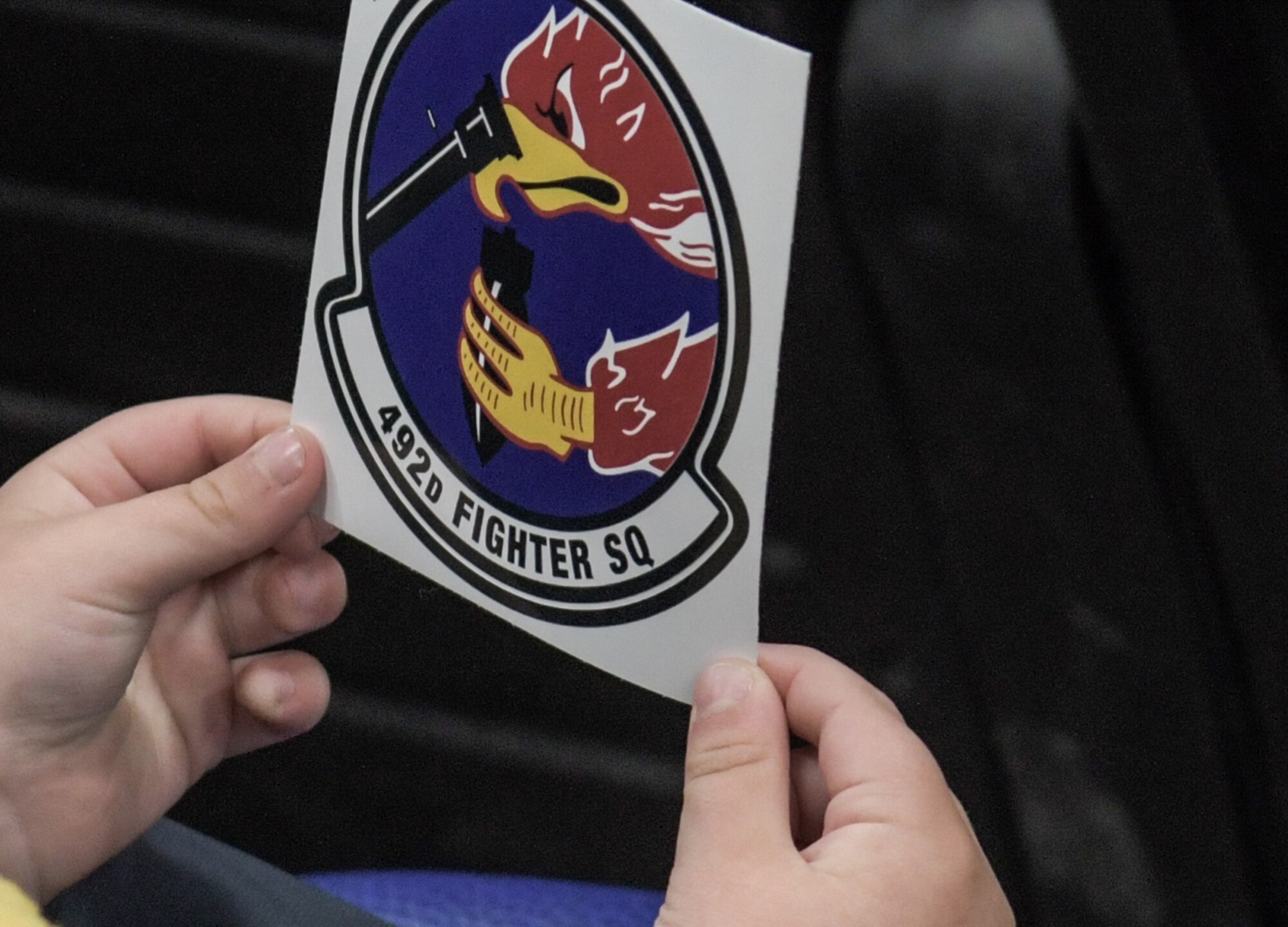 A child holds a sticker of the 492nd Fighter Squadron unit patch he received during a tour on April 15, 2021, at Royal Air force Lakenheath, England. The tour celebrates April as the Month of the Military Child highlights the experience of the dependent children of military members serving at home and overseas. (U.S. Air Force photo by Senior Airman Shanice Ship)