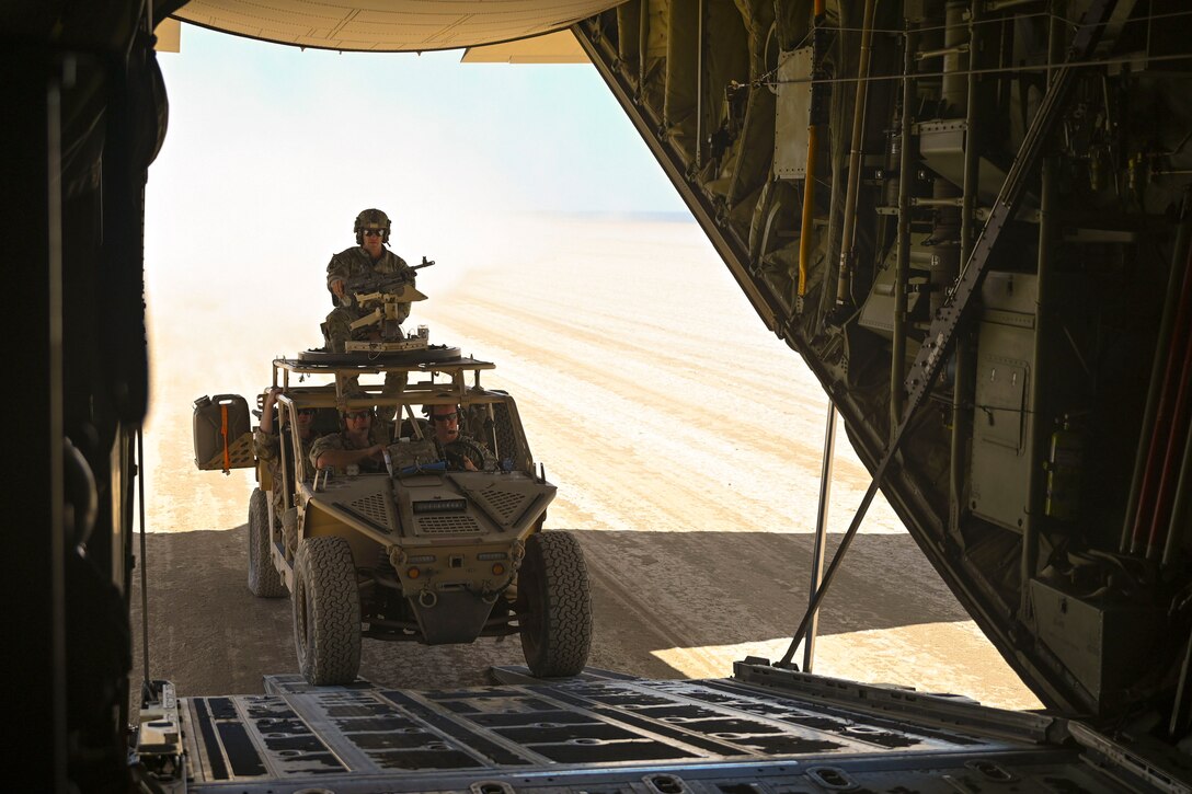 Airmen drive a tactical vehicle into an aircraft parked in a desert.