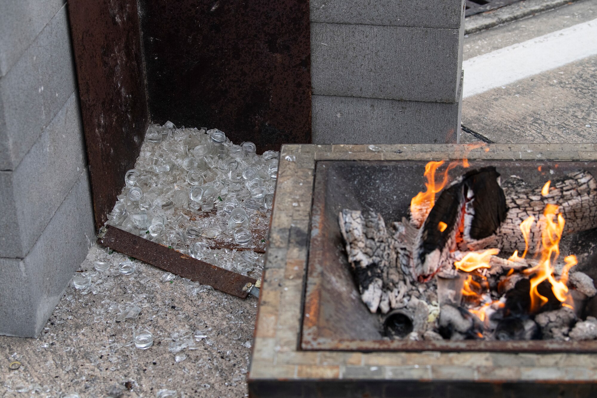 Broken shot glasses sit next to a ceremonial fire pit after a toast to fallen comrades