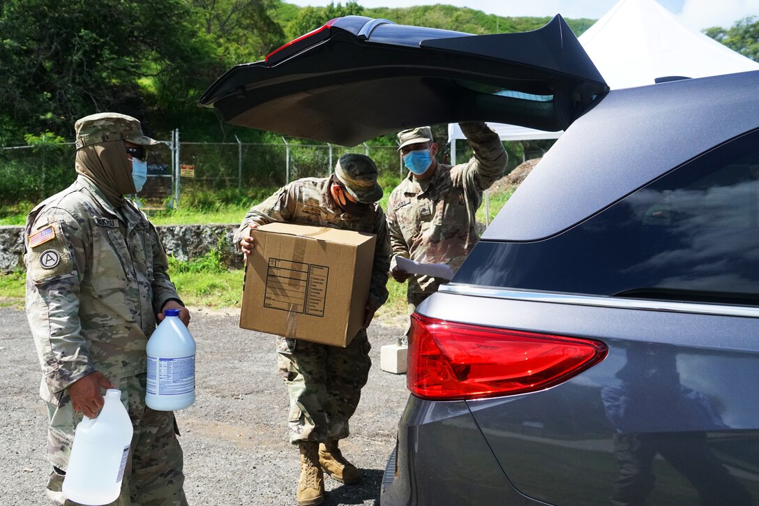 National Guard soldiers wearing face masks put boxes of personnel protective equipment, bottles of bleach and hand sanitizer into a vehicle.