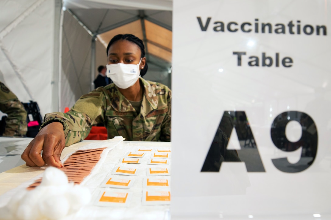 An airman wearing a face mask sets up a vaccine station.