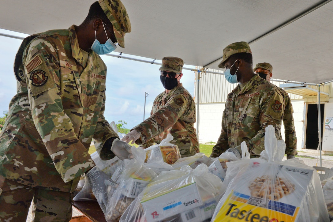 Airmen wearing face masks and gloves place bags of food on a table.