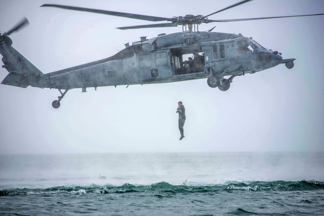 A search and rescue swimmer jumps from a Navy helicopter into water.