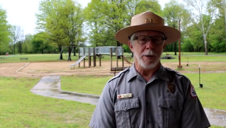 man in park ranger uniform standing in front of play ground equipment.