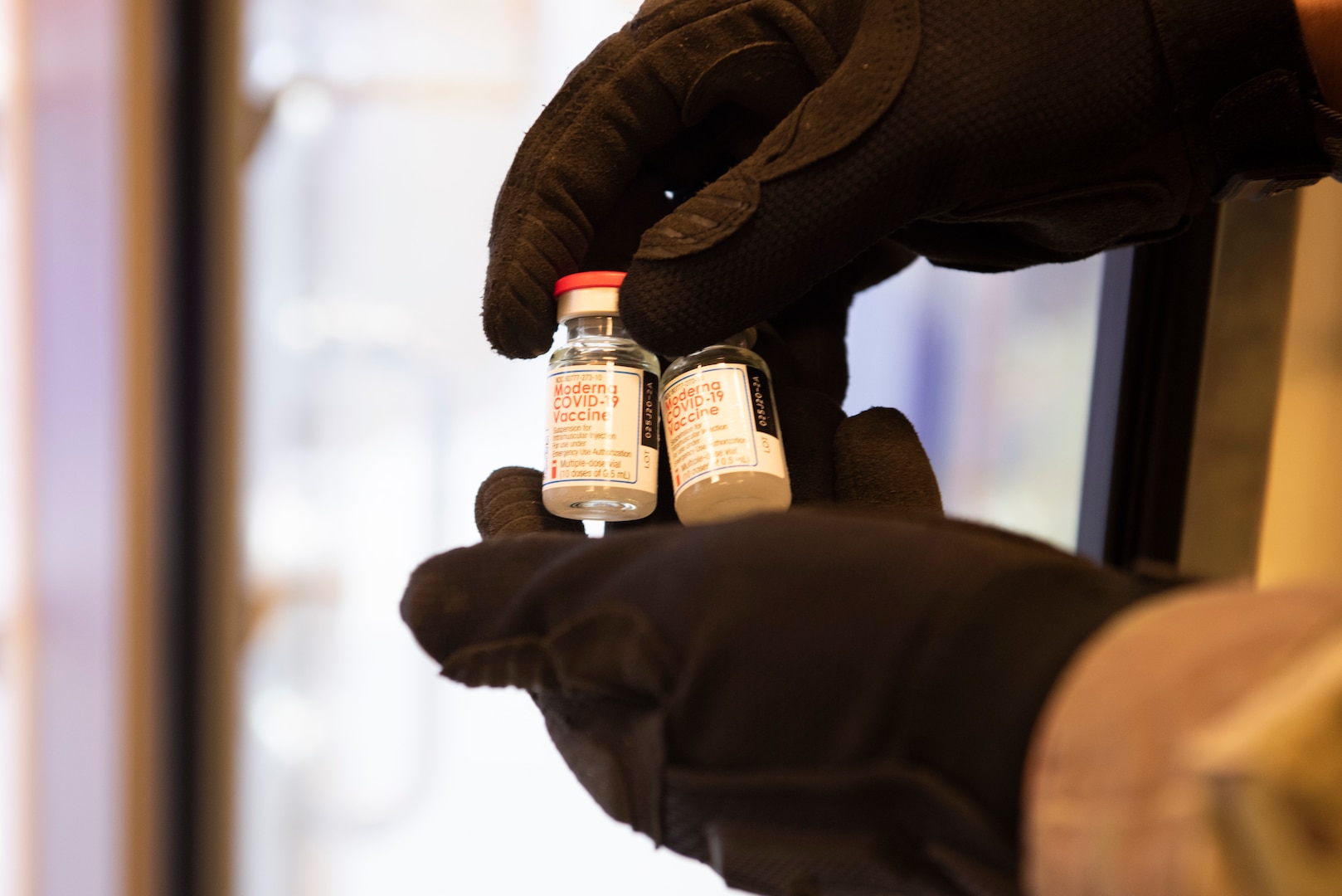 Two small bottles with labels are held by two hands in black gloves.