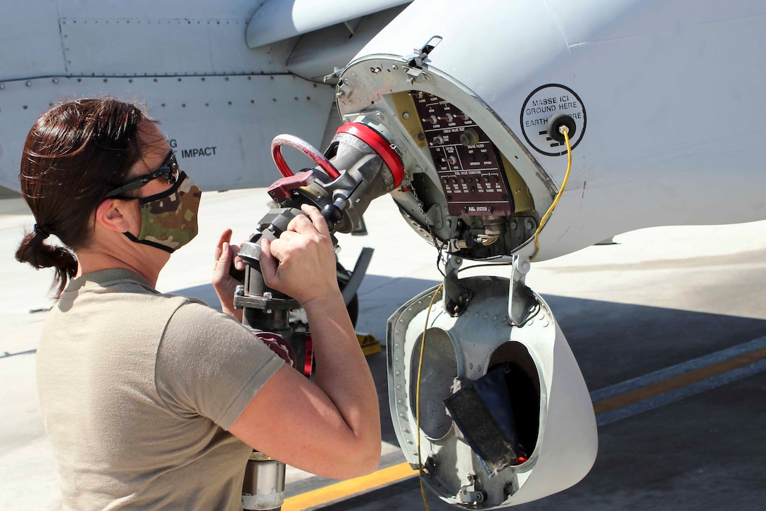 An airman holds a fuel hose next to an aircraft.