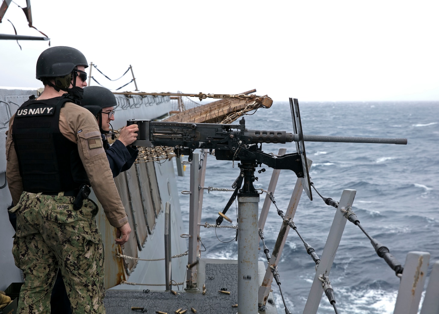 Logistics Specialist 3rd Class Aaron Scott, left, and Gunner's Mate 2nd Class Dylan Harris assigned to the amphibious transport dock ship USS San Antonio (LPD 17) watches as Scott fires a M-2 .50 caliber machine gun during a live-fire exercise on the ship's flight deck, April 1, 2021.