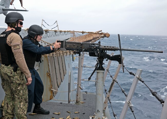 Seaman Ethan Valentine , right, and Gunner's Mate 2nd Class Dylan Harris assigned to the amphibious transport dock ship USS San Antonio (LPD 17) watches as Valentine fires a M-2 .50 caliber machine gun on the ship's flight deck, April 1, 2021.