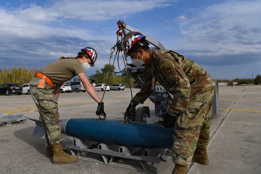 U.S. Airmen with the 31st Munitions Squadron (MUNS) hook an inert bomb onto a bomb lift at Andravida Air Base, Greece, April 13, 2021. The 31st MUNS, along with other units from the 31st Fighter Wing, participated in INIOCHOS 21, a Hellenic air force-led, joint force exercise. (U.S. Air Force photo by Airman 1st Class Thomas S. Keisler IV)