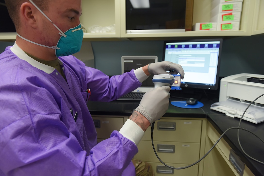 An airman in medical gear and gloves works in a lab.