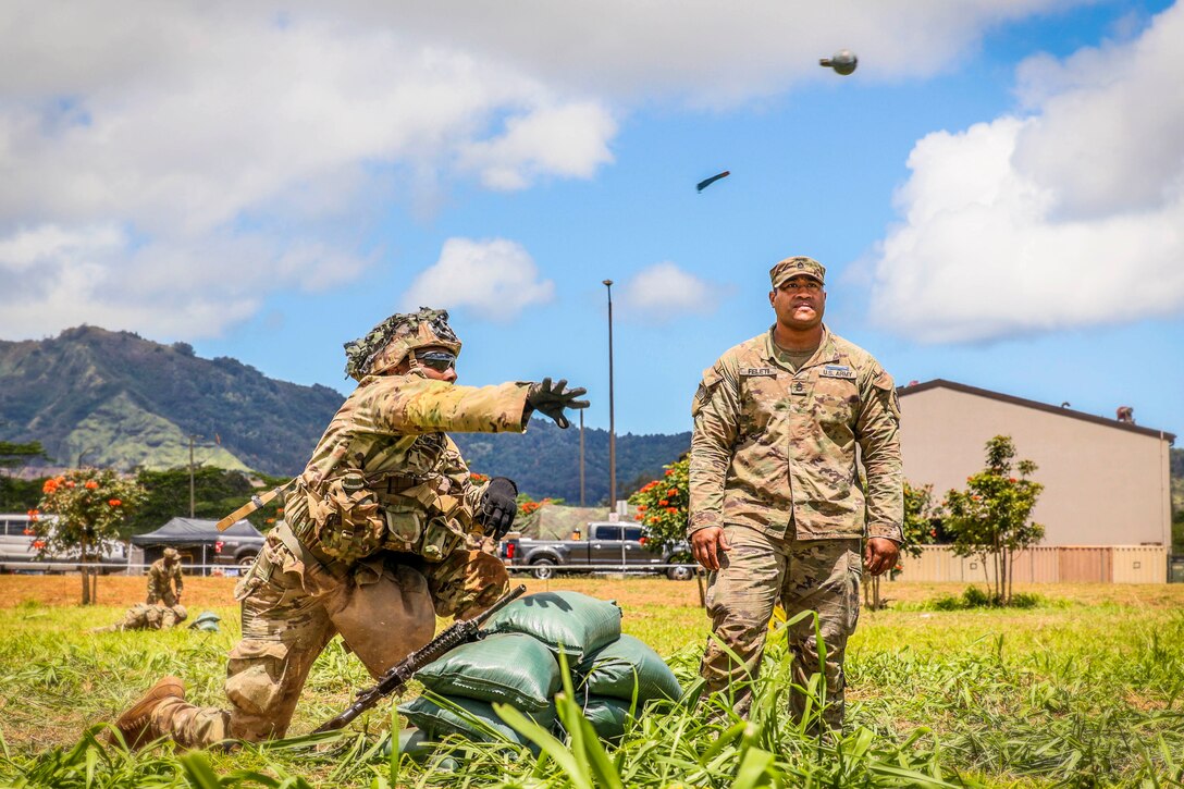 A soldier throws a grenade while a fellow soldier watches.