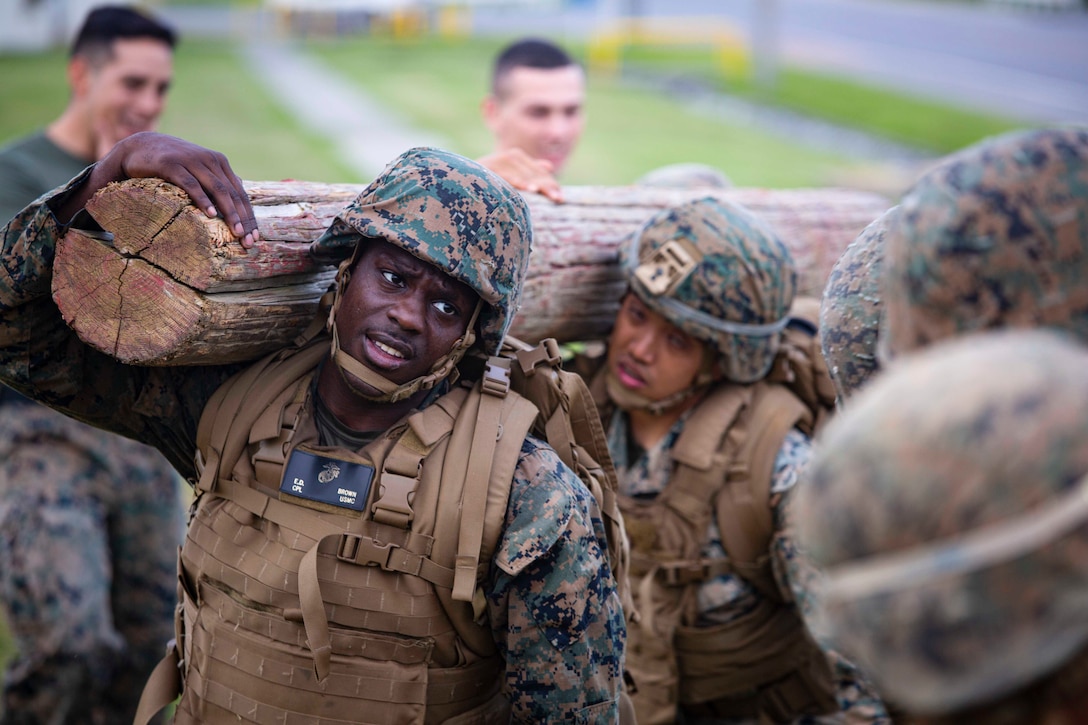 Marines carry a log as others watch.