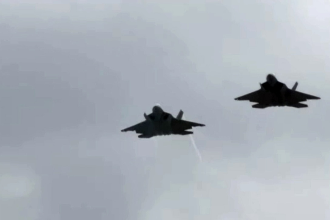 Two military aircraft fly together through an overcast sky.