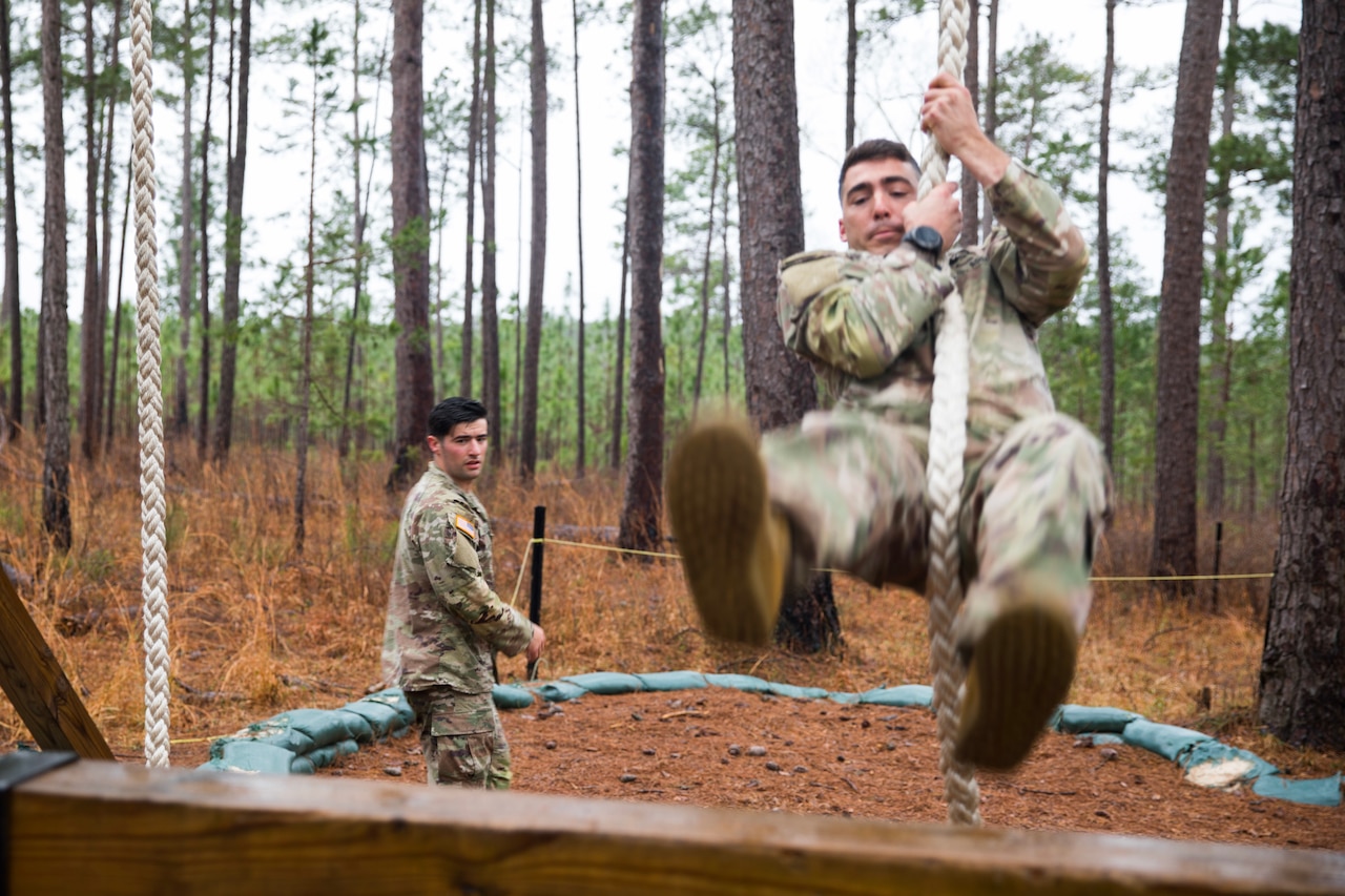A soldier swings forward from a rope. Another soldier looks on in the background.