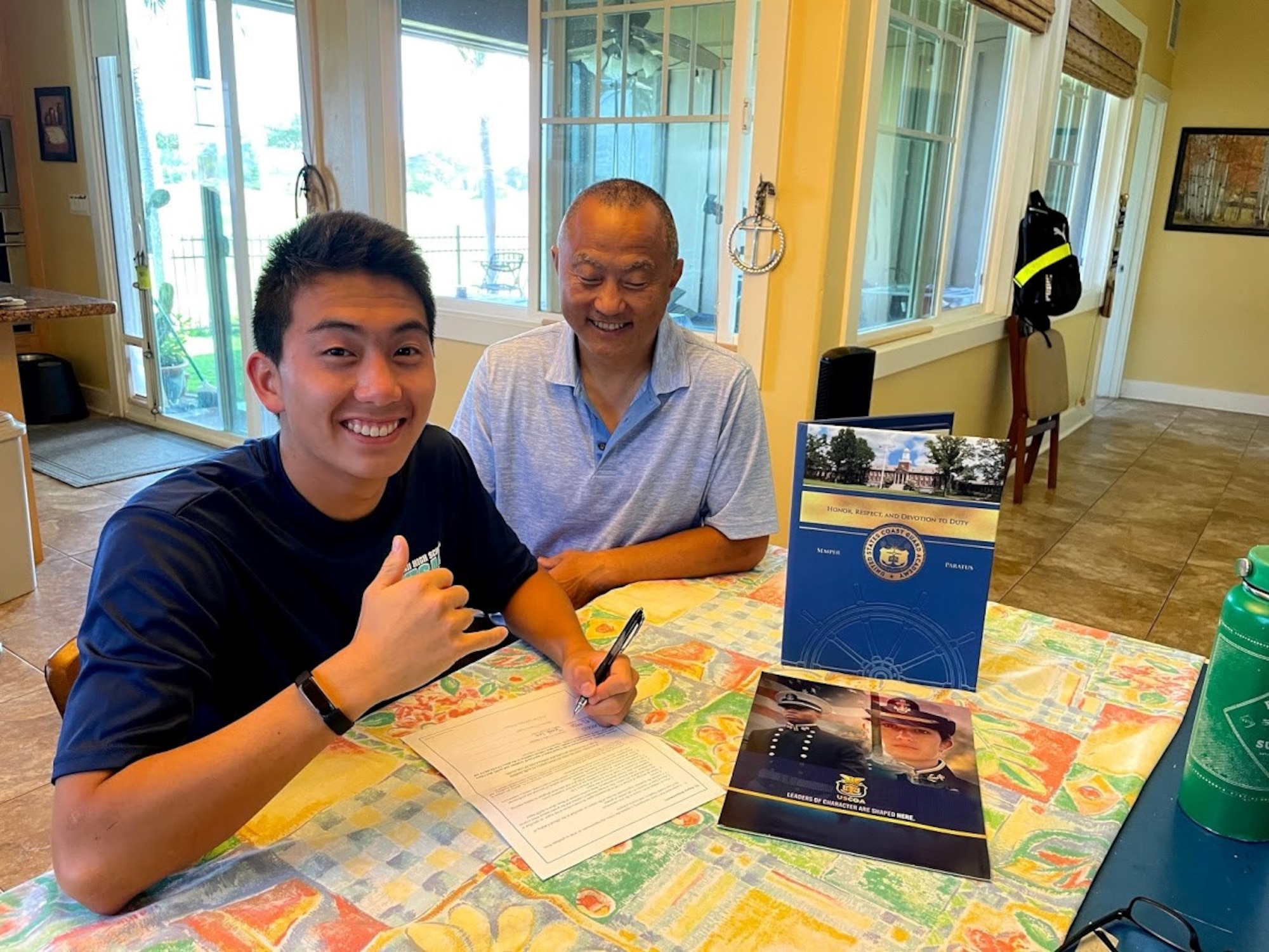 Jonah Lee, high school senior, signs his acceptance into the U.S. Coast Guard Academy alongside his father, U.S. Navy Capt. Benjamin Lee, Naval Health Clinic Hawaii family physician. Jonah grew up as a military child and looks forward to remaining in the military community after enjoying the bonds he made growing up. Jonah also looks forward to serving his country and caring for the environment. (Courtesy photo)