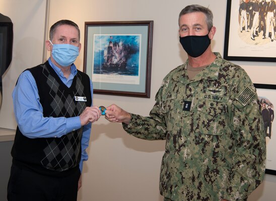 Newport, R.I. (April 13, 2021) Rear Adm. Pete Garvin, commander, Naval Education and Training Command, right, presents Jim Jacobs, a Naval Supply Corps School instructor, with a command coin during a visit to Naval Station (NAVSTA) Newport R.I., April 13. While onboard NAVSTA Newport, Garvin also visited Center for Service Support, Naval Chaplaincy School and Center, Surface Warfare Schools Command, and the Senior Enlisted Academy.  (U.S. Navy photo by Mass Communication Specialist 2nd Class Derien C. Luce)