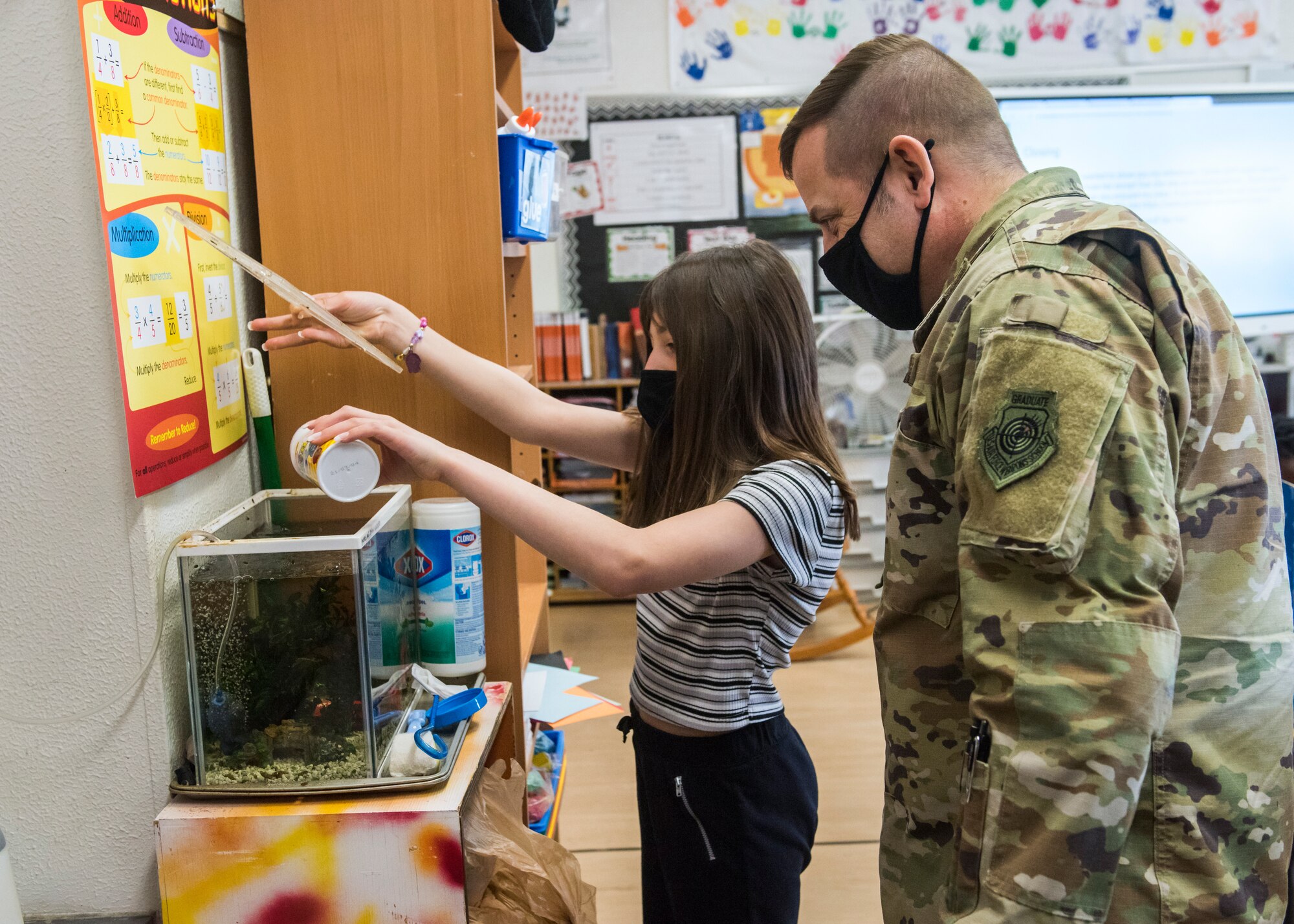 Man in uniform watches student feed a fish.