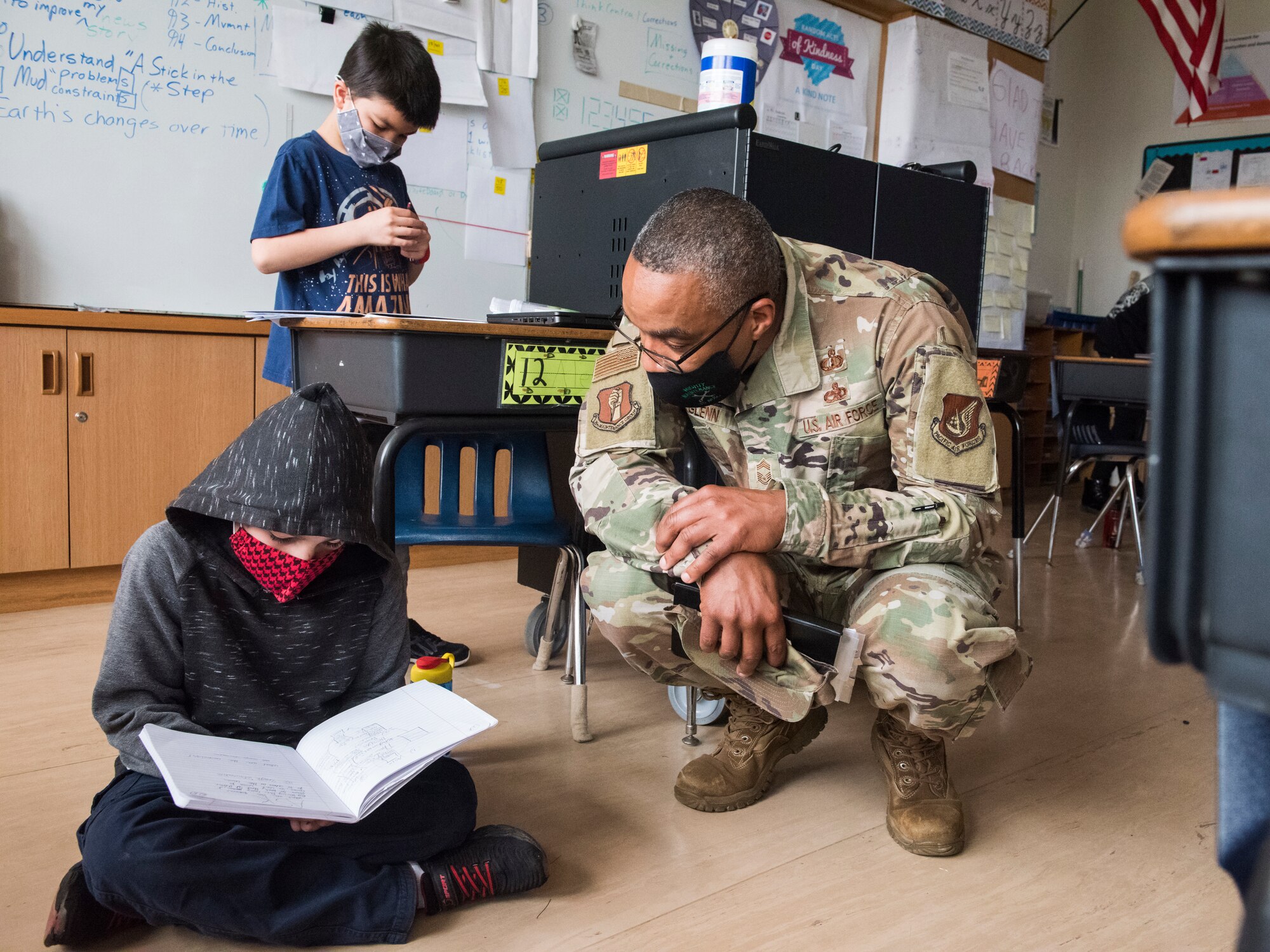 Man in uniform kneels down next to child reading notebook